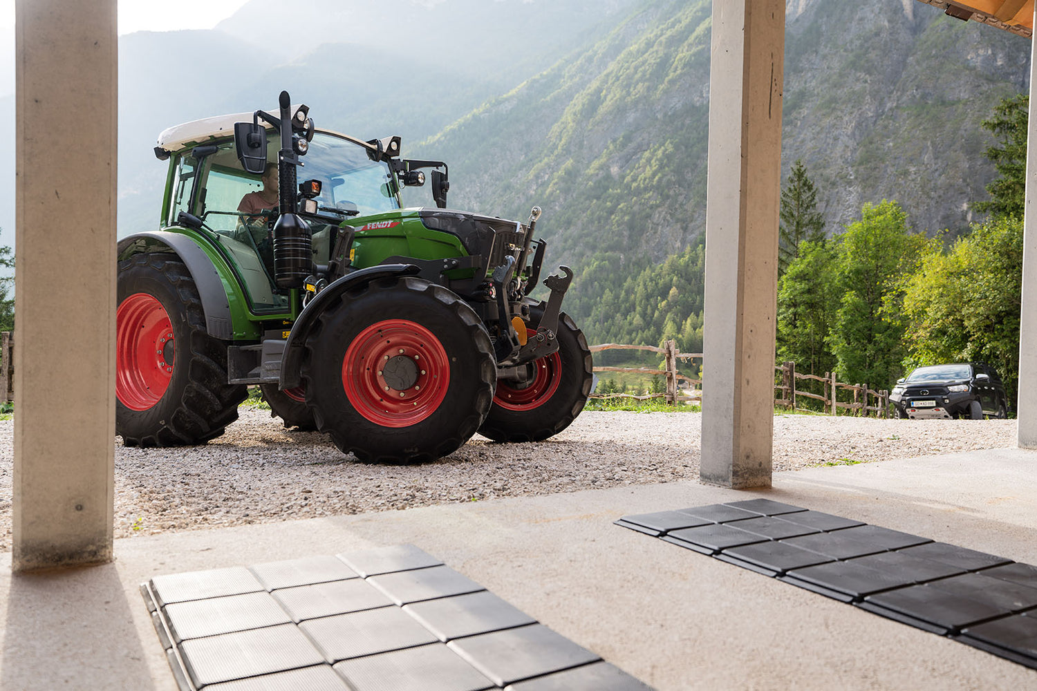 Zeleni traktor Fendt se vozi proti garaži po pohodnih ploščah za zaščito tal.