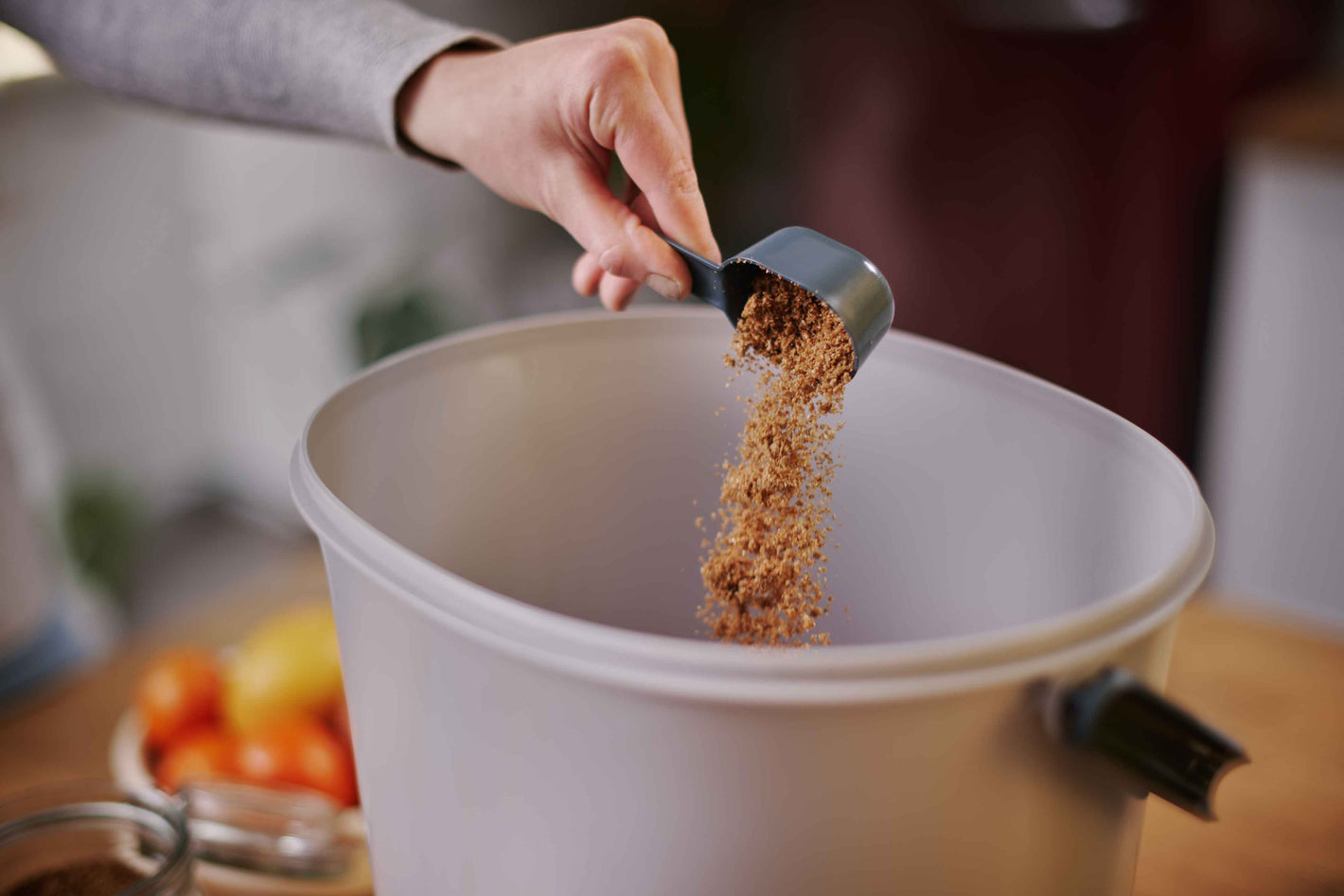 Roka s priloženo zajemalko posipa dodaja posip v Bokashi Organko Essential kompostnik.