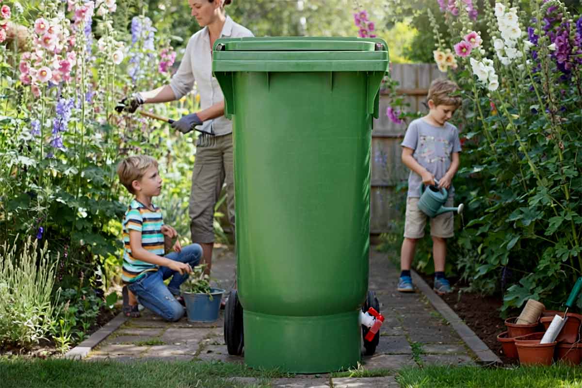Organko XL kompostnik na vrtu, družina odlaga biološke odpadke.